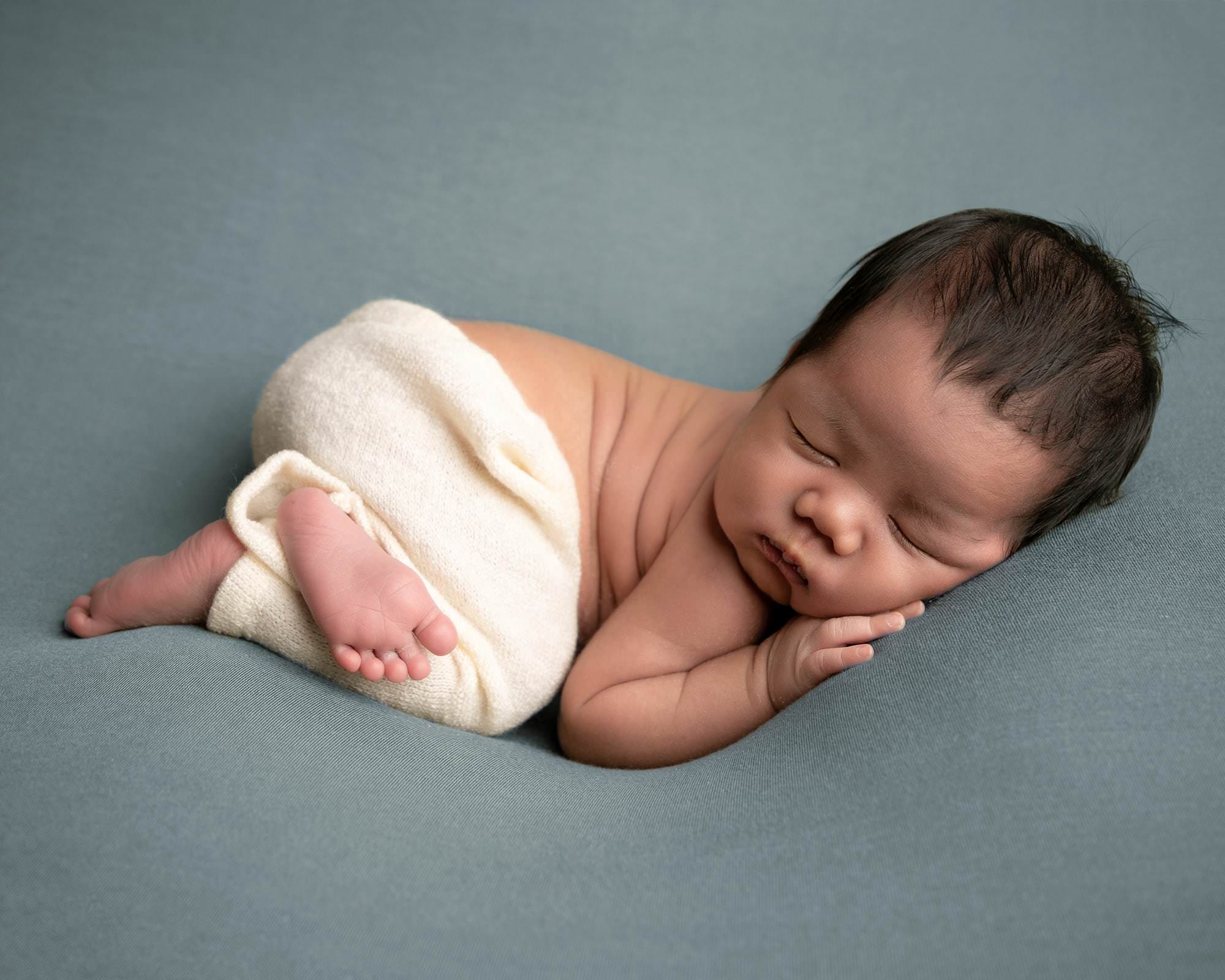 Baby boy lying on his tummy wearing cream trousers. Image captured in Glasgow during newborn photography session