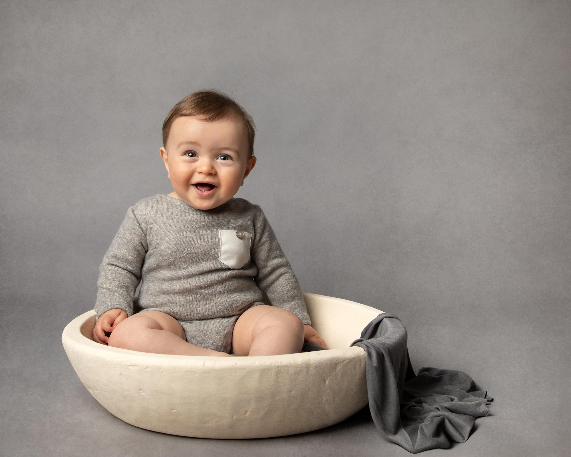 Baby in cream bowl wearing grey romper with Glasgow baby photographer