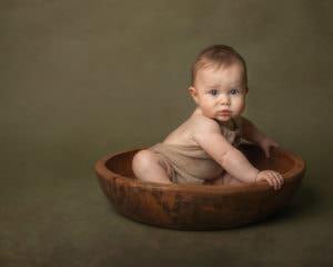Baby in wooden bowl on green backdrop during baby photography session