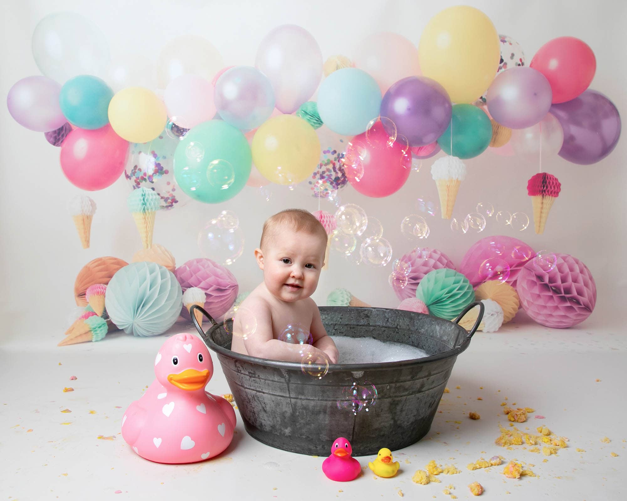Baby girl in bath with bubbles & balloon backdrop during 1st birthday cakesmash photoshoot in Glasgow