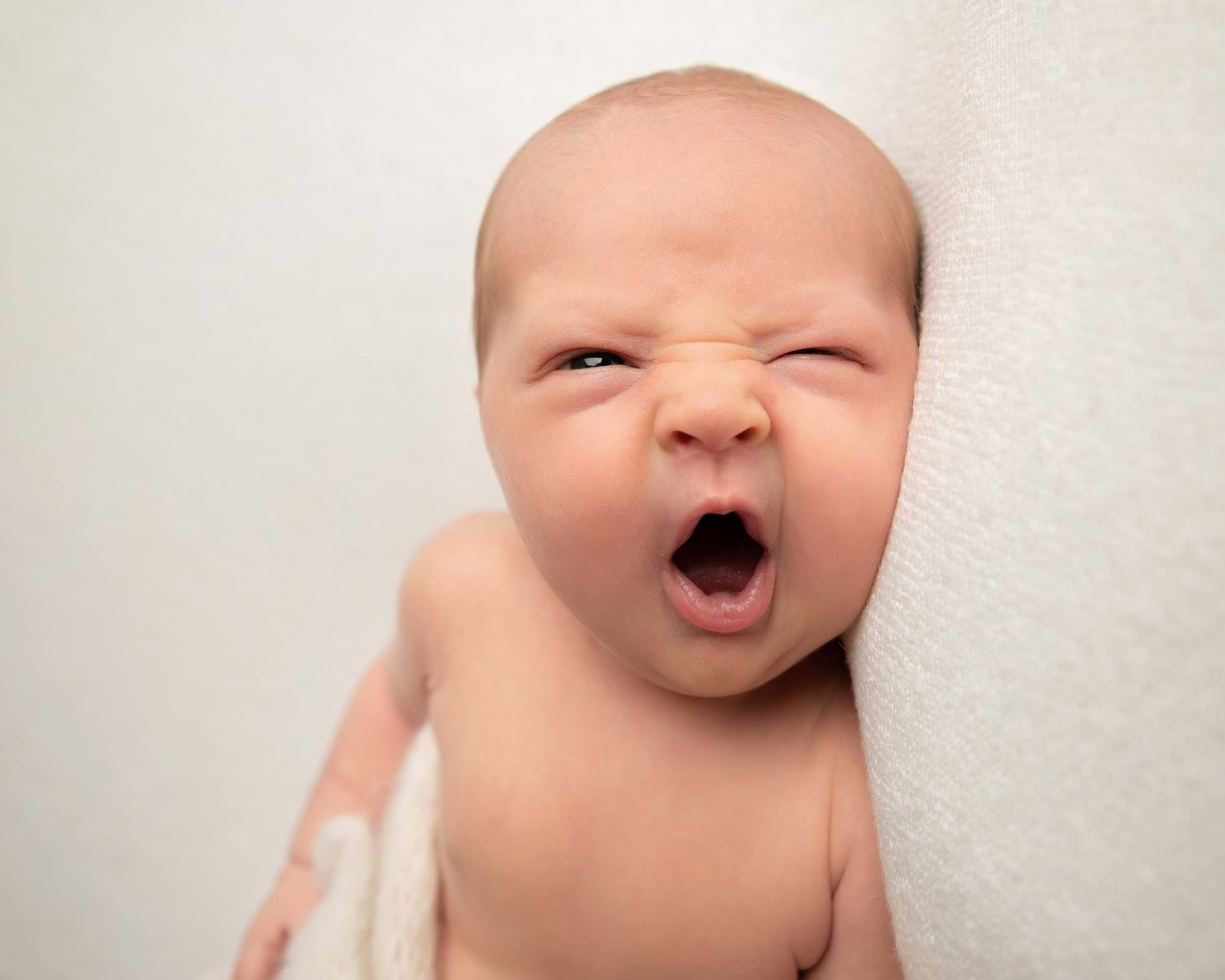 Image during Glasgow Baby Photoshoot of a baby on a cream blanket. Close up shot of baby yawning