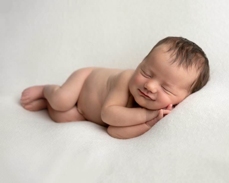 Baby girl on cream blanket, lying on her side smiling.