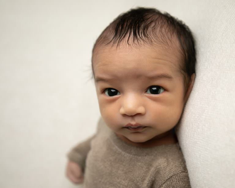Baby boy in beige romper on cream blanket eyes open. Part of a gallery from newborn photography shoot in Glasgow