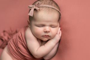 Close up of baby girl on pink blanket with both hand together resting under her face. Image part of newborn photography session in Glasgow