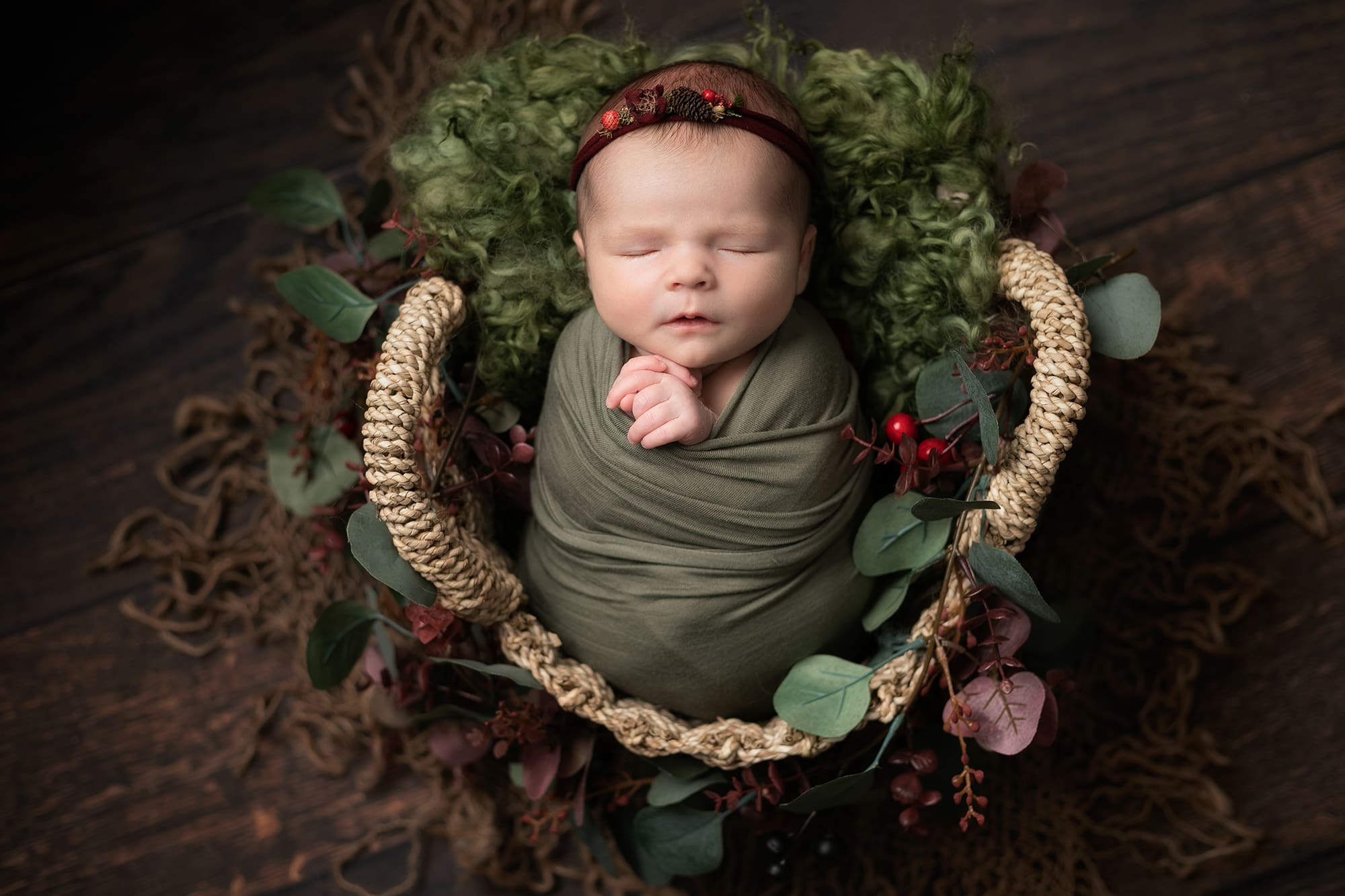 Baby girl swaddled in green wrap in a basket i festive set up during newborn photoshoot