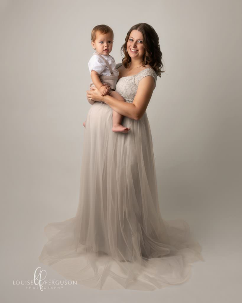 Pregnant female is cream gown holding toddler boy around her baby bump. Part of a gallery of images included in maternity photography session in Glasgow
