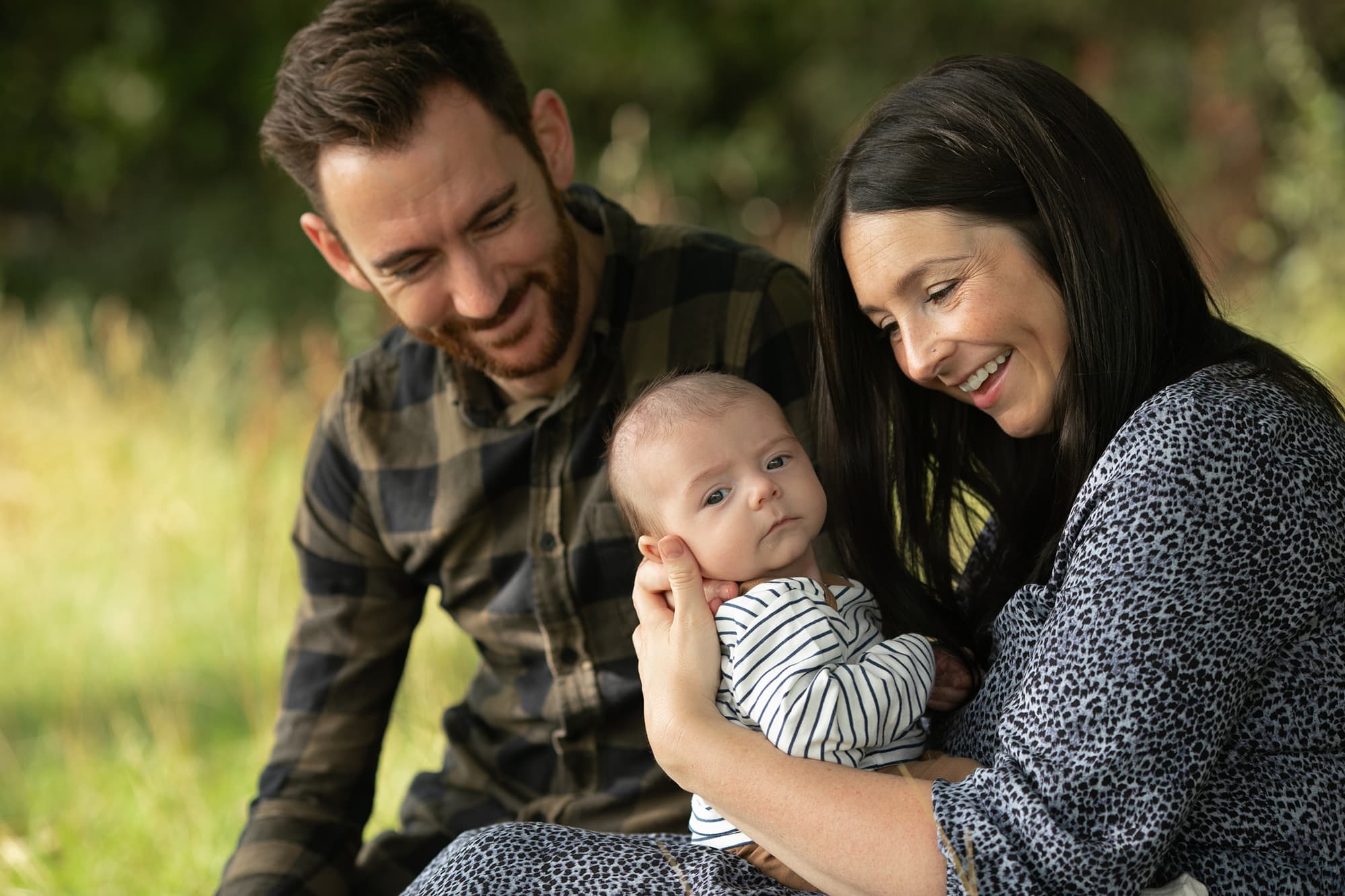 Mum & dad sat with baby in long grass. Image captured by Glasgow photographer during family photography session