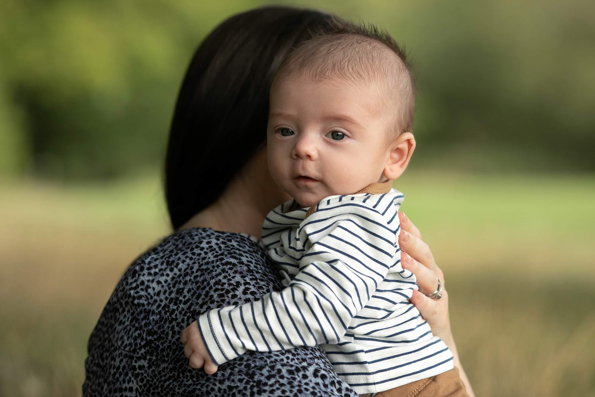 Baby boy being held by mum and looking out from her shoulder. Image taken by Glasgow Photographer at outdoor family photography session
