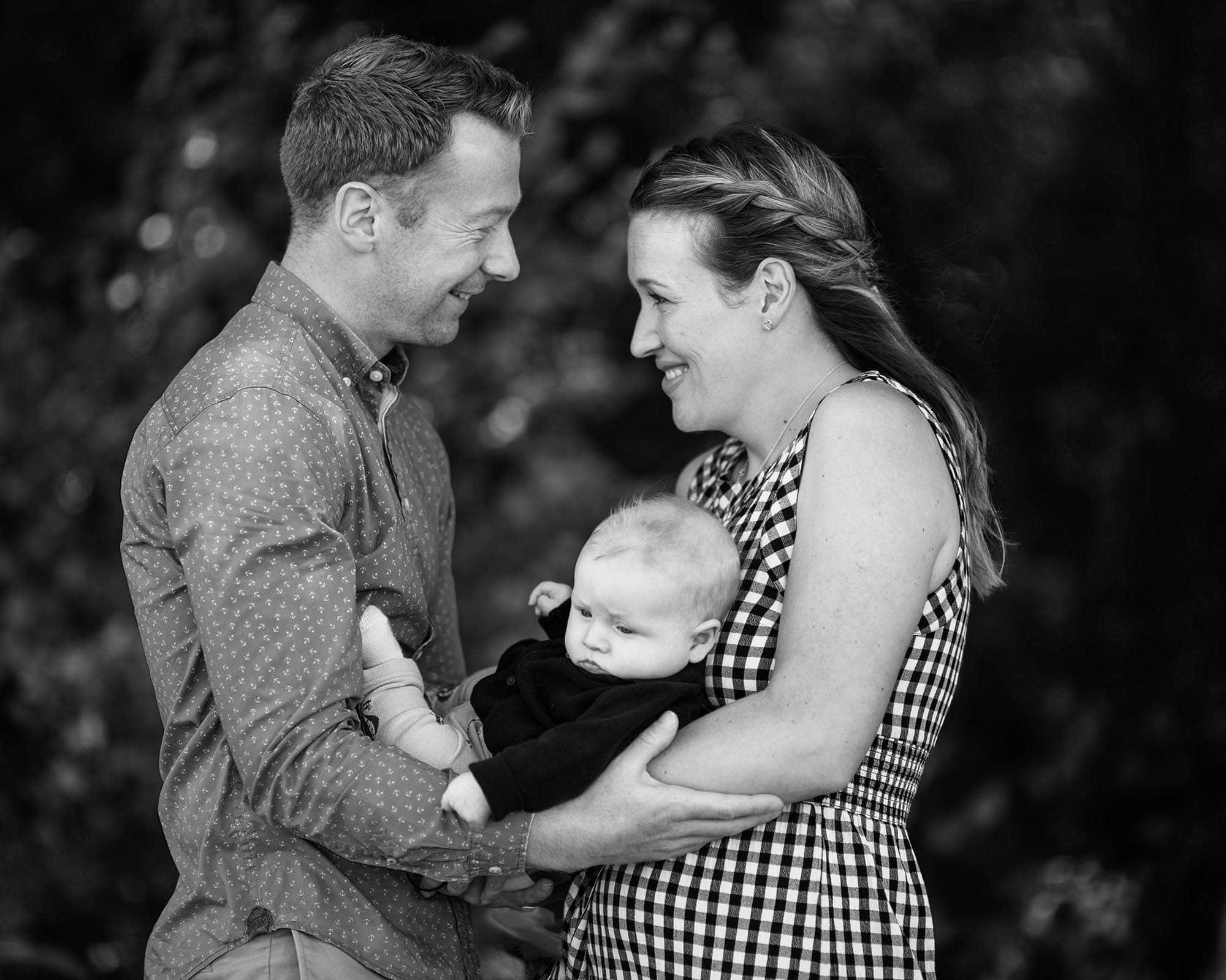 Black & White image offparents holding baby, facing each other and smiling at one and other.
