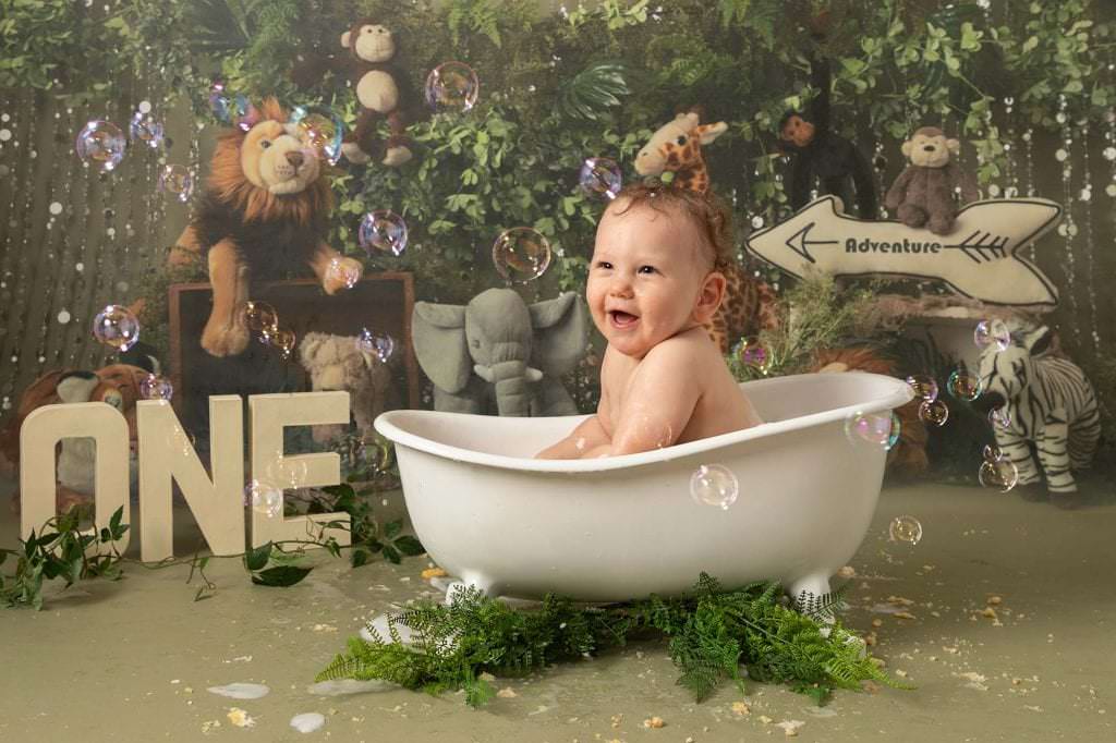 Baby boy sat in white roll top bath with jungle scene behind. Image taken following 1st birthday photoshoot in glasgow