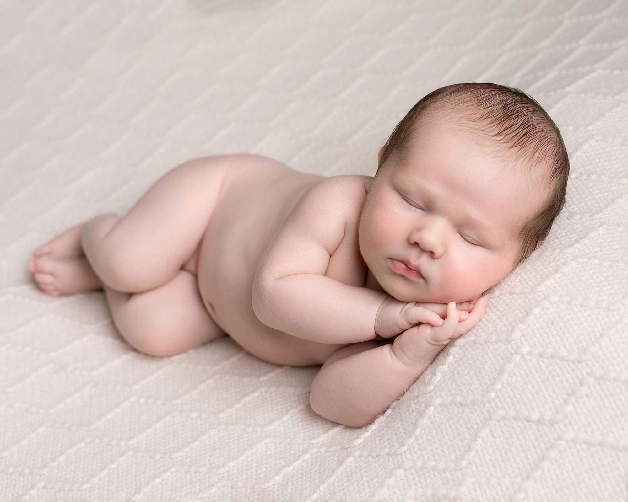 Baby boy lying on his side on a cream backdrop. Image taken as part of a newborn mini photoshoot gallery