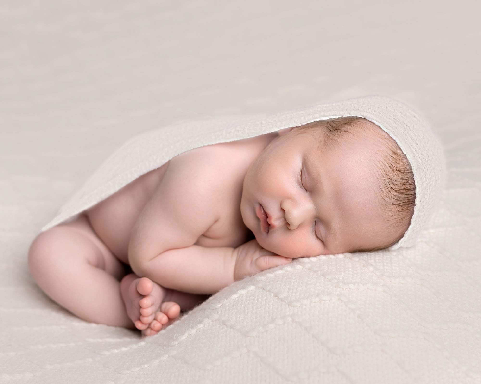 Baby on a cream backdrop in taco pose with a cream wrap over him, taken by local newborn photographer near me. taken at a newborn mini photoshoot