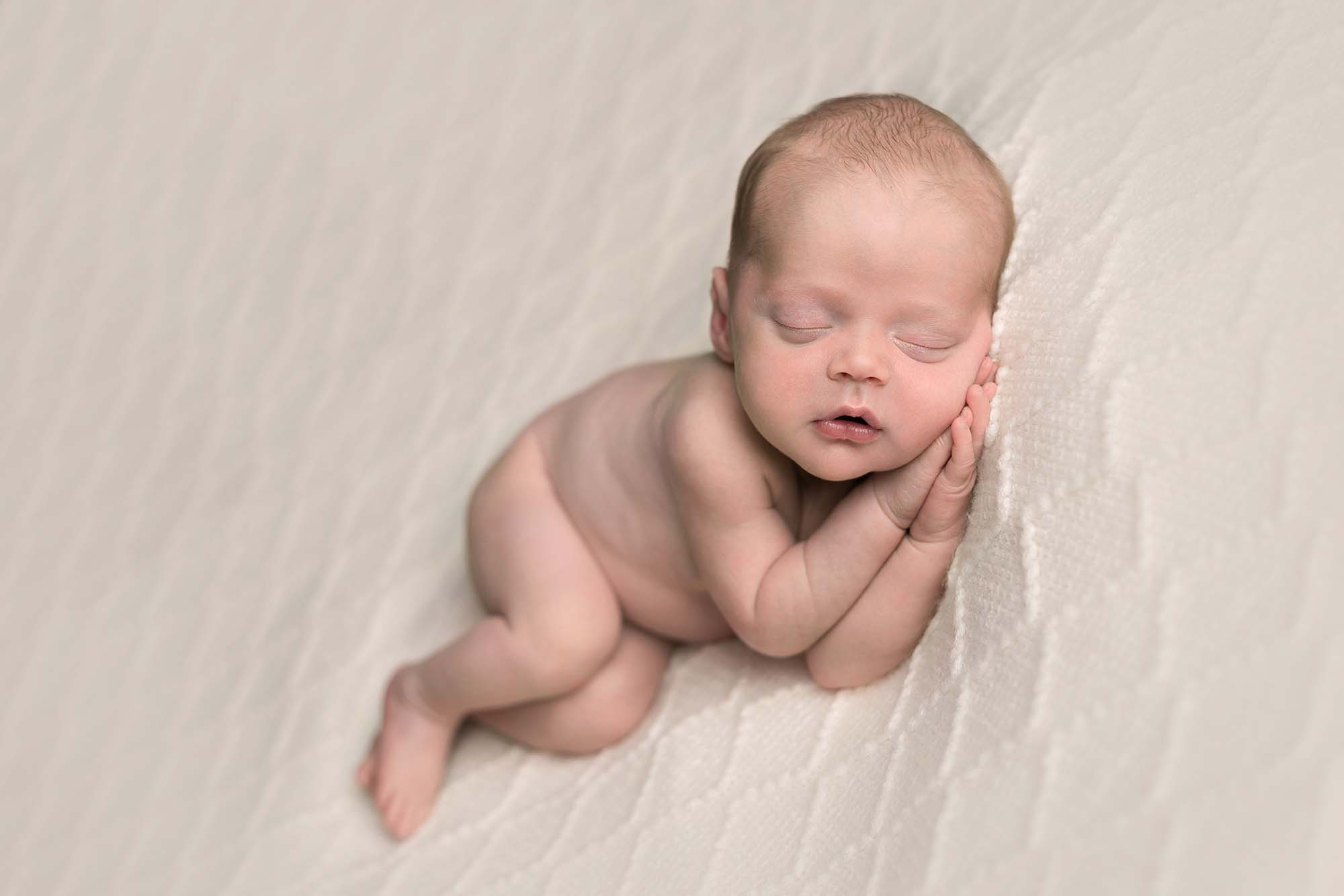 Baby lying on his side on a diamond cream blanket sleeping. Image taken by Newborn photographer in Glasgow during baby photoshoot