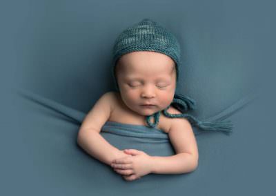 Baby boy tucked in on blue blanket with matching bonnet by Newborn Photographer Glasgow