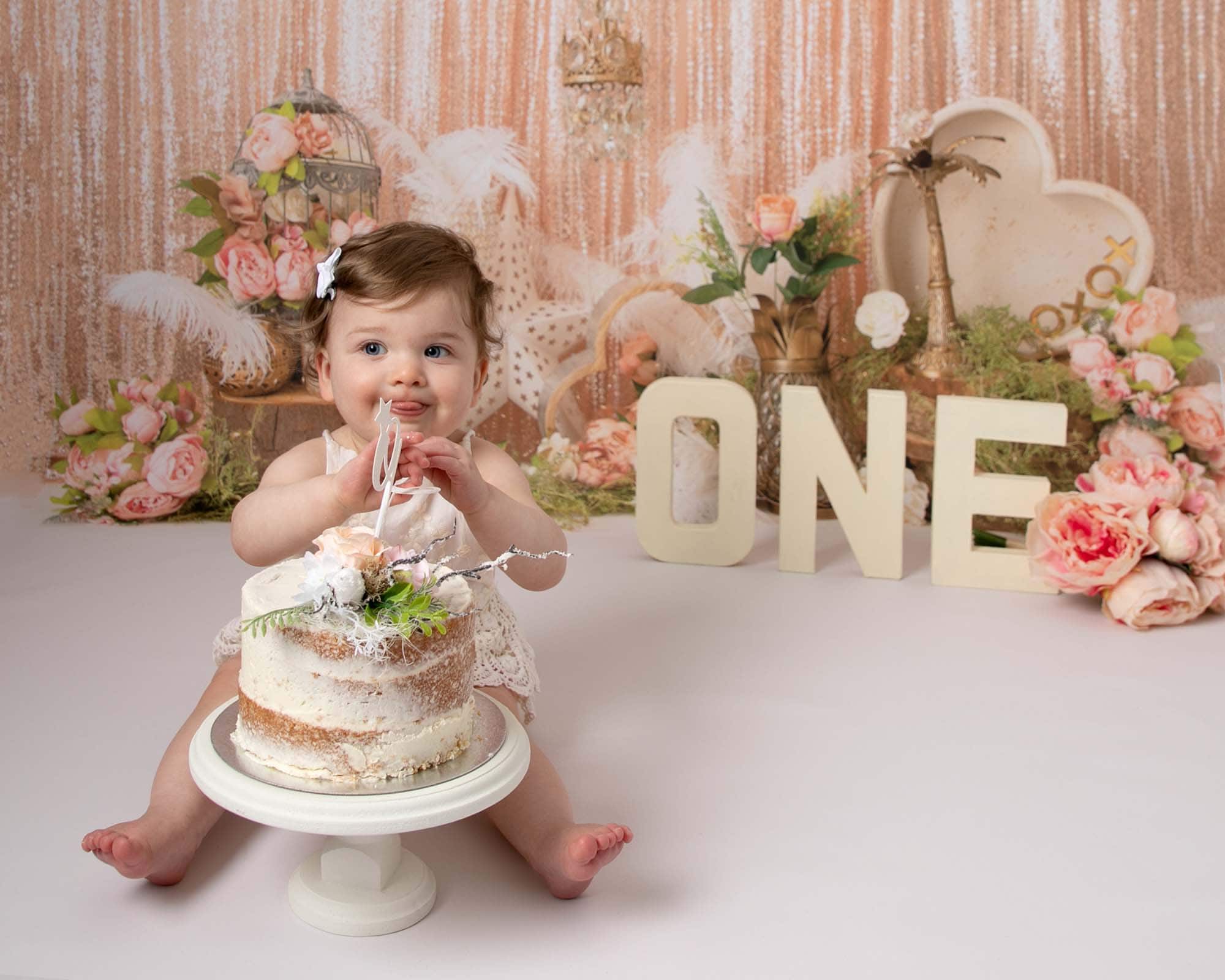 Baby girl sitting with a cake on a boho peach backdrop at her 1st birthday photoshoot in Glasgow