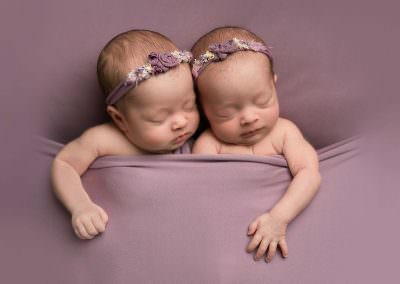 Newborn twin girls wrapped in purple ounder a purple blanket asleep. Image taken at Newborn Baby photography Glasgow