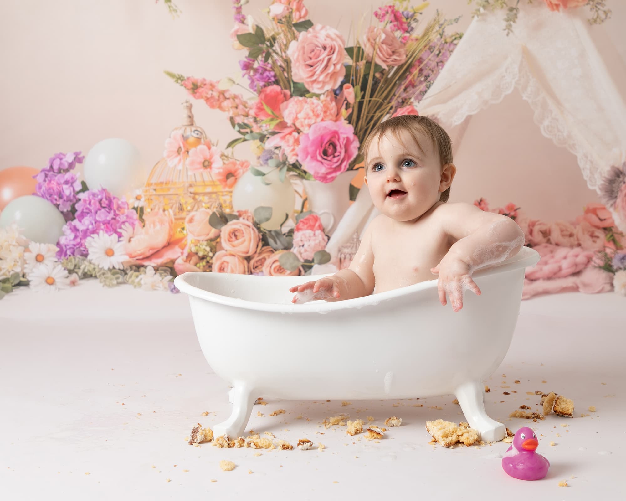 Baby girl in a mini white bathtub. Backdrop of floral arrangement and a teepee