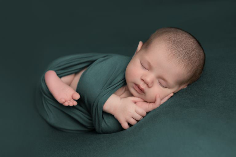 Baby boy on jade green blanket wrapped for his newborn photography session. baby is sleeping
