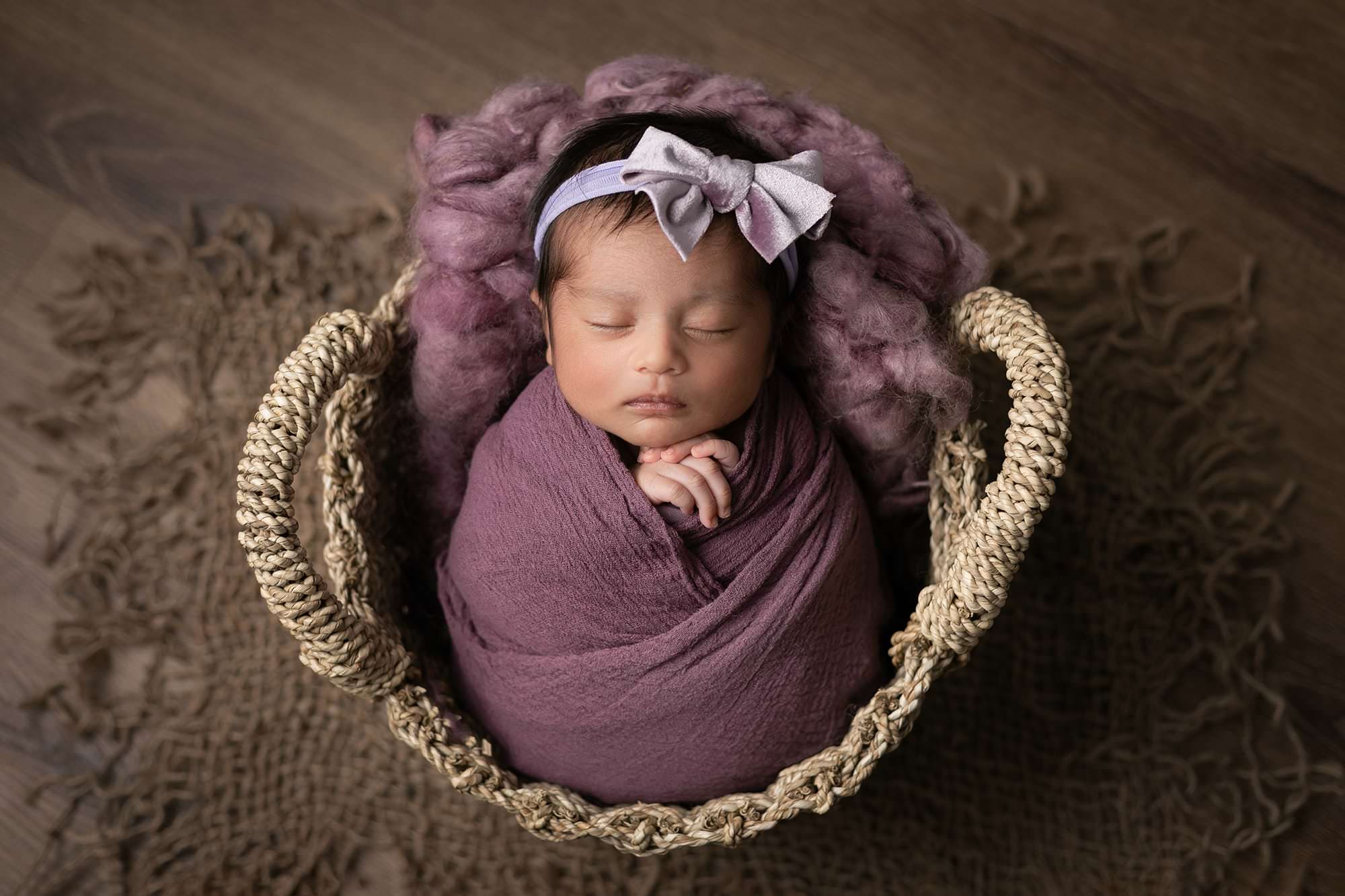 Baby in a round basket, wrapped in purple wrap, with her head looking upwards. Image taken by Glasgow newborn Photographer