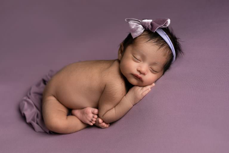 Baby girl lying o her side sleeping on dusty lavanedar blanket as part of her newborn photography gallery