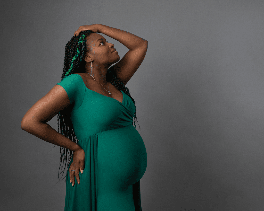 Side view of pregnant woman wearing jade green dress, with braids in her hair. Image taken during maternity Photography session in Glasgow
