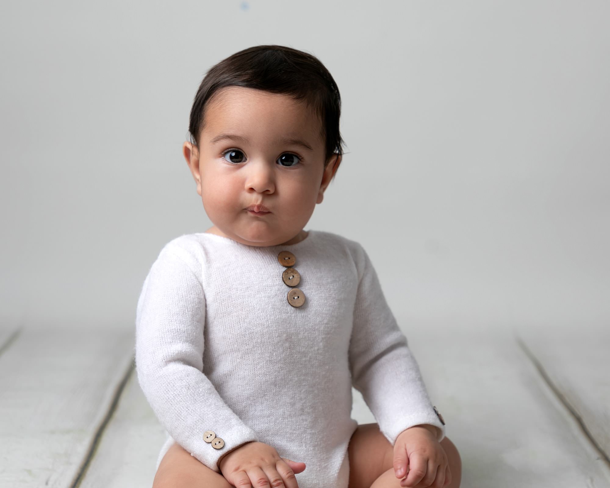 Baby boy in white romper on cream wooden backdrop. Image taken at photoshoot with Glasgow Baby Photographer