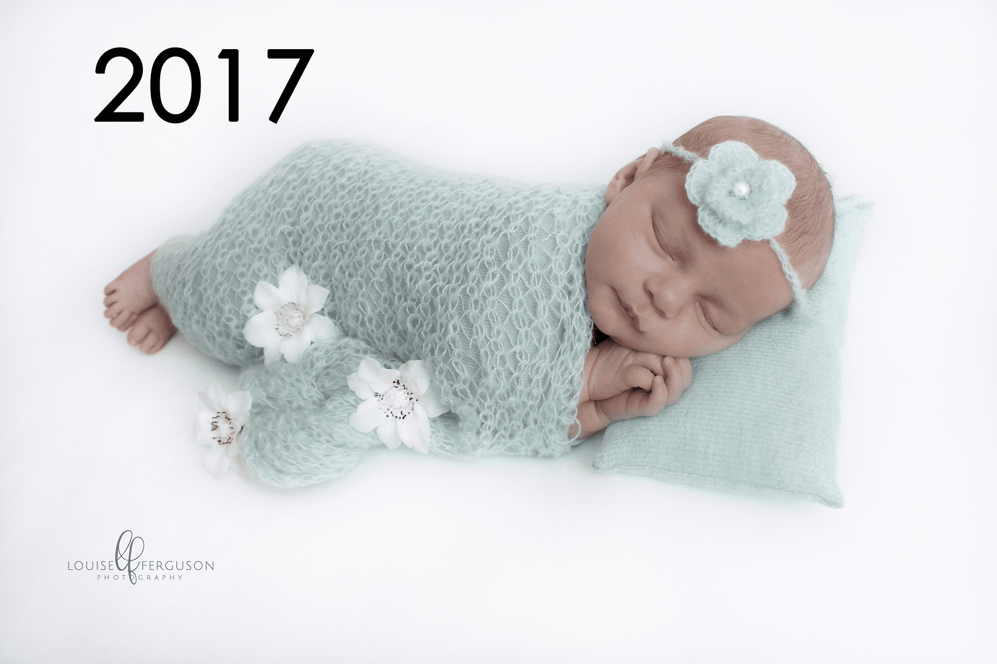 An example of an image taken in the first year of training as a newborn photographer. Baby girl wrapped in green on white backdrop lying on her side