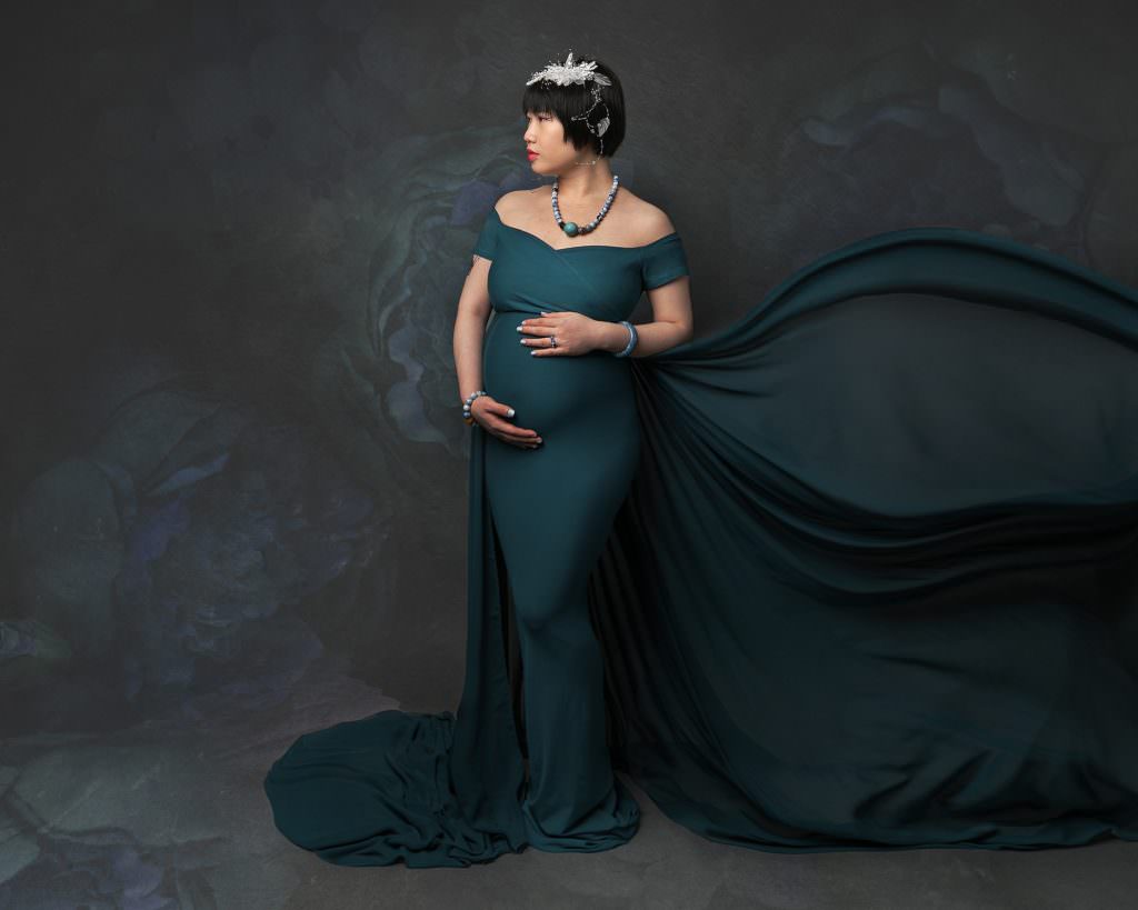 Image of a pregnant woman taken at a maternity photography session in Glasgow. Woman wears a green gown with flowing train. Short dark hair and profile view