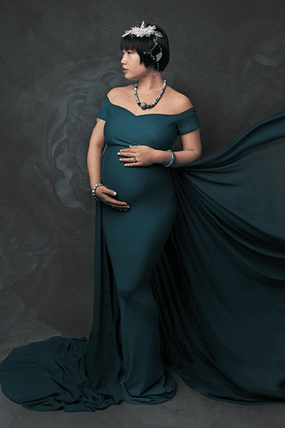 Image of a pregnant woman taken at a maternity photography session in Glasgow. Woman wears a green gown with flowing train. Short dark hair and profile view